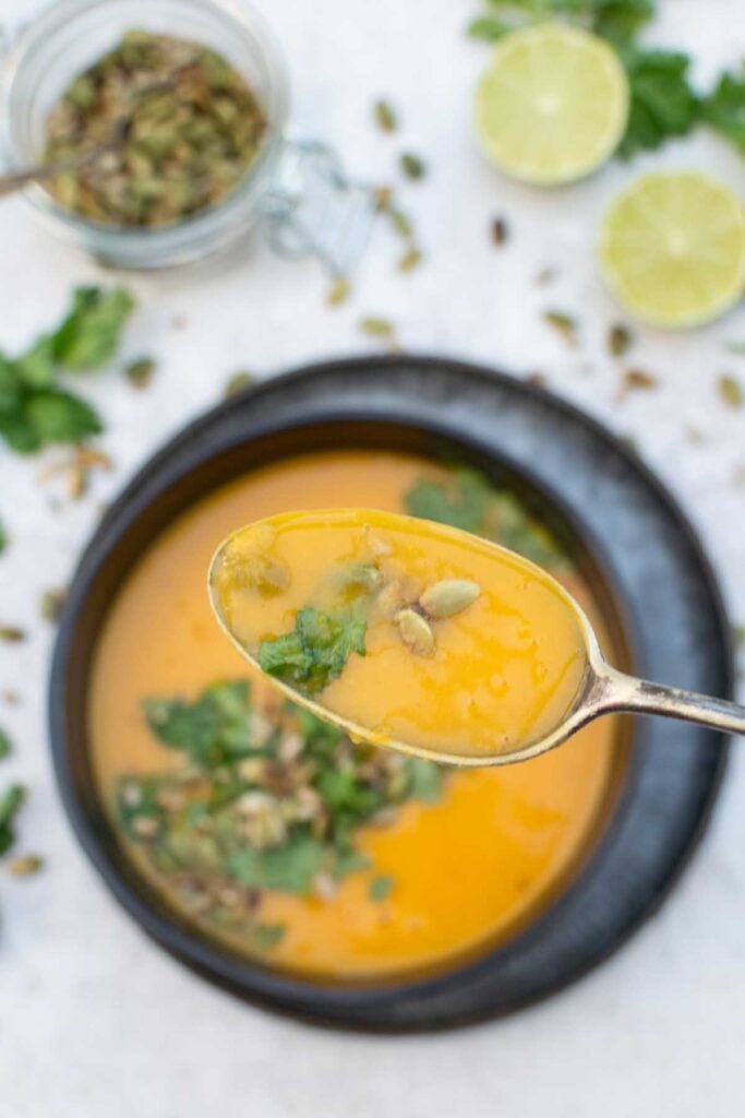 Spoonful of creamy Thai pumpkin soup with coriander and pumpkin seeds, lifted from a bowl of the soup