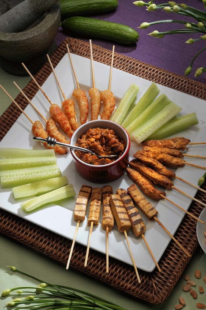 Vegan chicken, shrimp and cucumber satay skewers on a platter around a bowl of satay peanut sauce